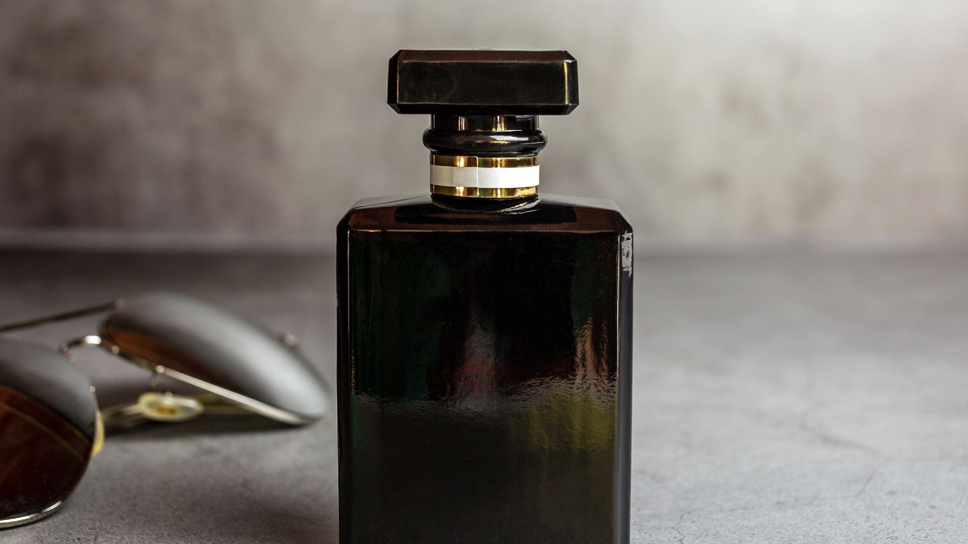Ciemny flakon perfum na szarym tle z okularami przeciwsłonecznymi